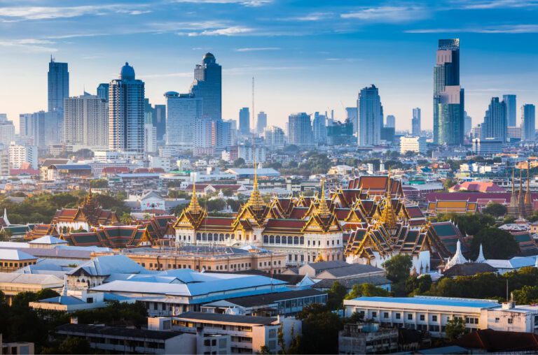 Panoramic view of the Bangkok skyline, featuring a mix of modern skyscrapers, bustling high-rise buildings, and a vibrant cityscape under a partly cloudy sky.